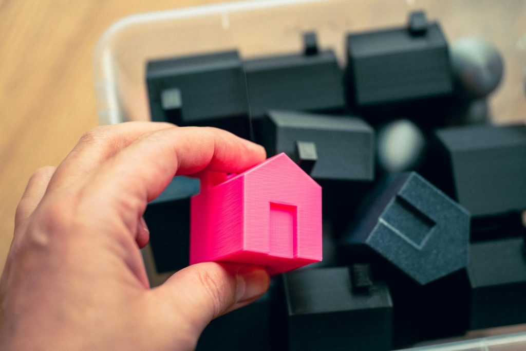 Die Auswahl eines rosafarbenen Hausmodells aus einer Schachtel mit Miniaturhäusern symbolisiert die Wahlmöglichkeiten im Immobilienbereich.